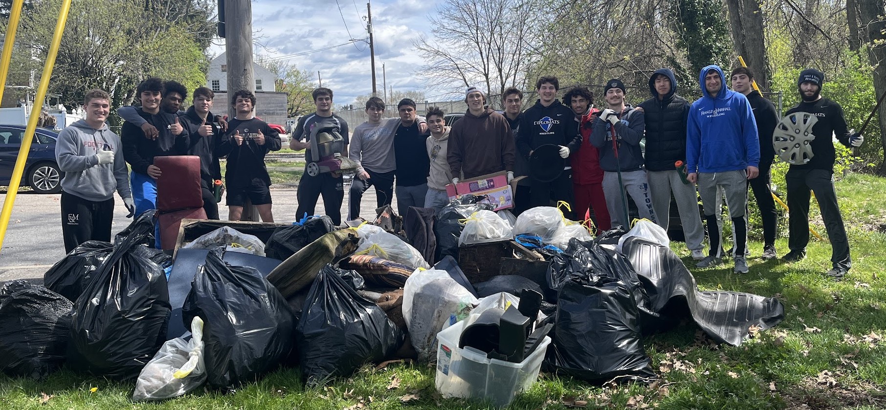 A group of volunteers poses with their collection of trash bags in the foreground. 